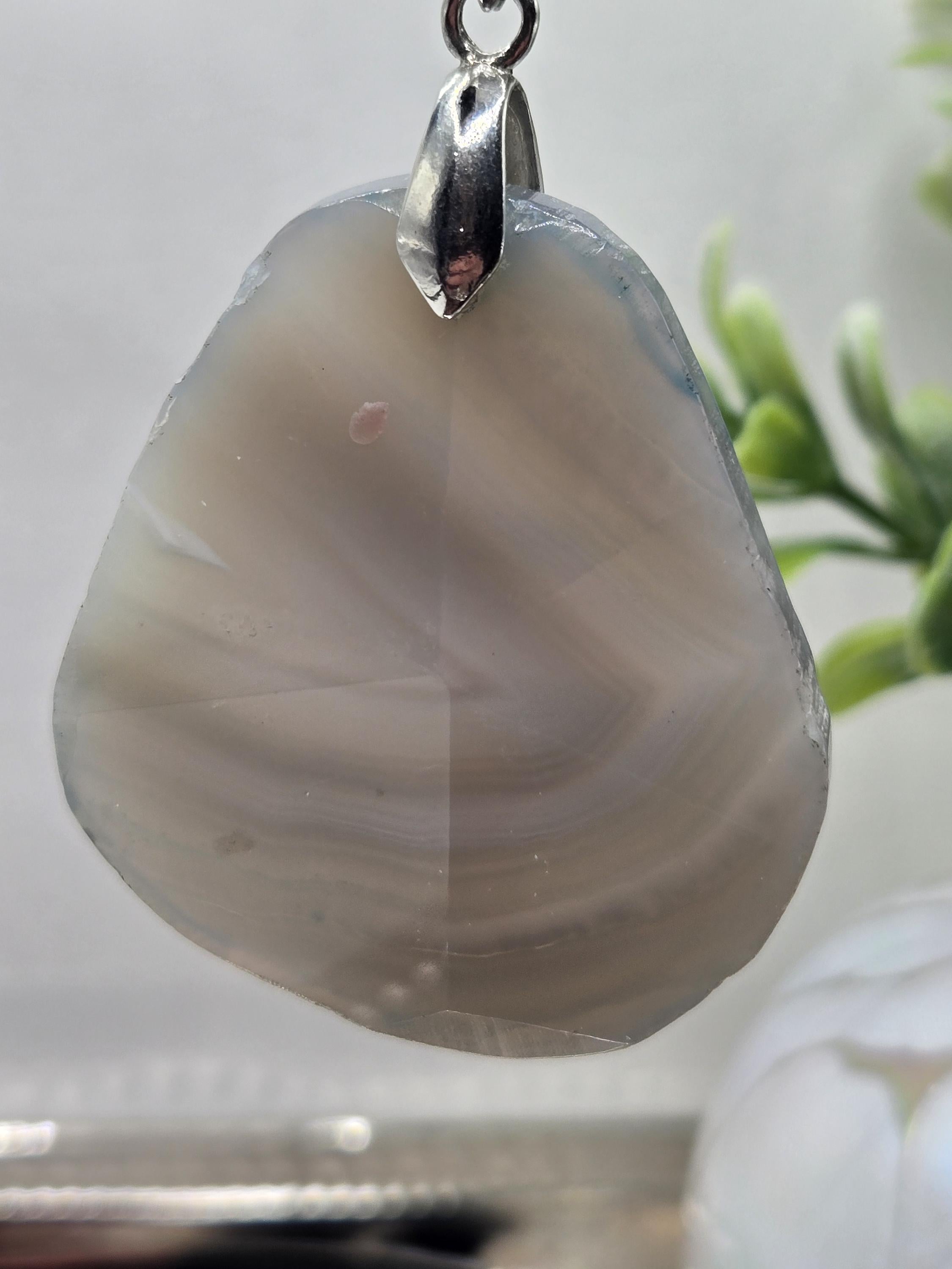 A close-up image of a pendant with a unique, striped stone-like shape, possibly a piece of agate or a similar type of rock.