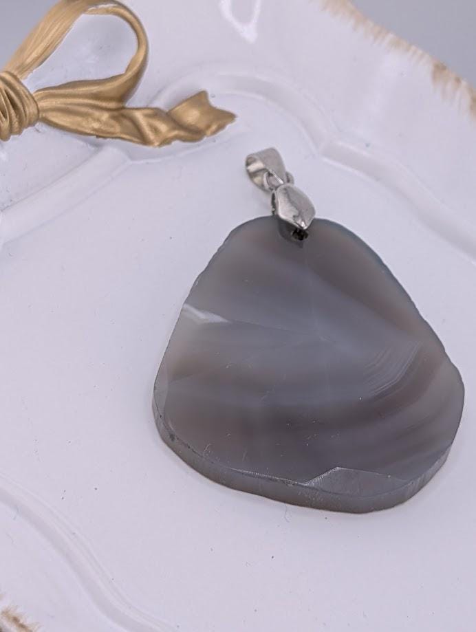 A large, irregularly shaped, gray stone pendant with a metal clasp is displayed on a white surface.