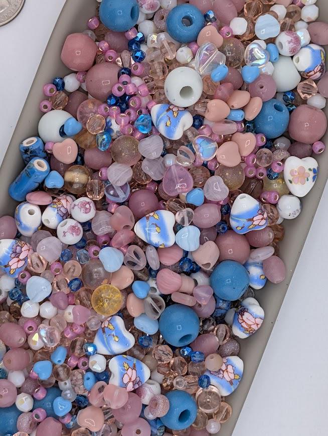 A colorful assortment of glass beads in various shapes, sizes, and colors, including blue, pink, white, and multicolored beads, creating a visually appealing and diverse display.