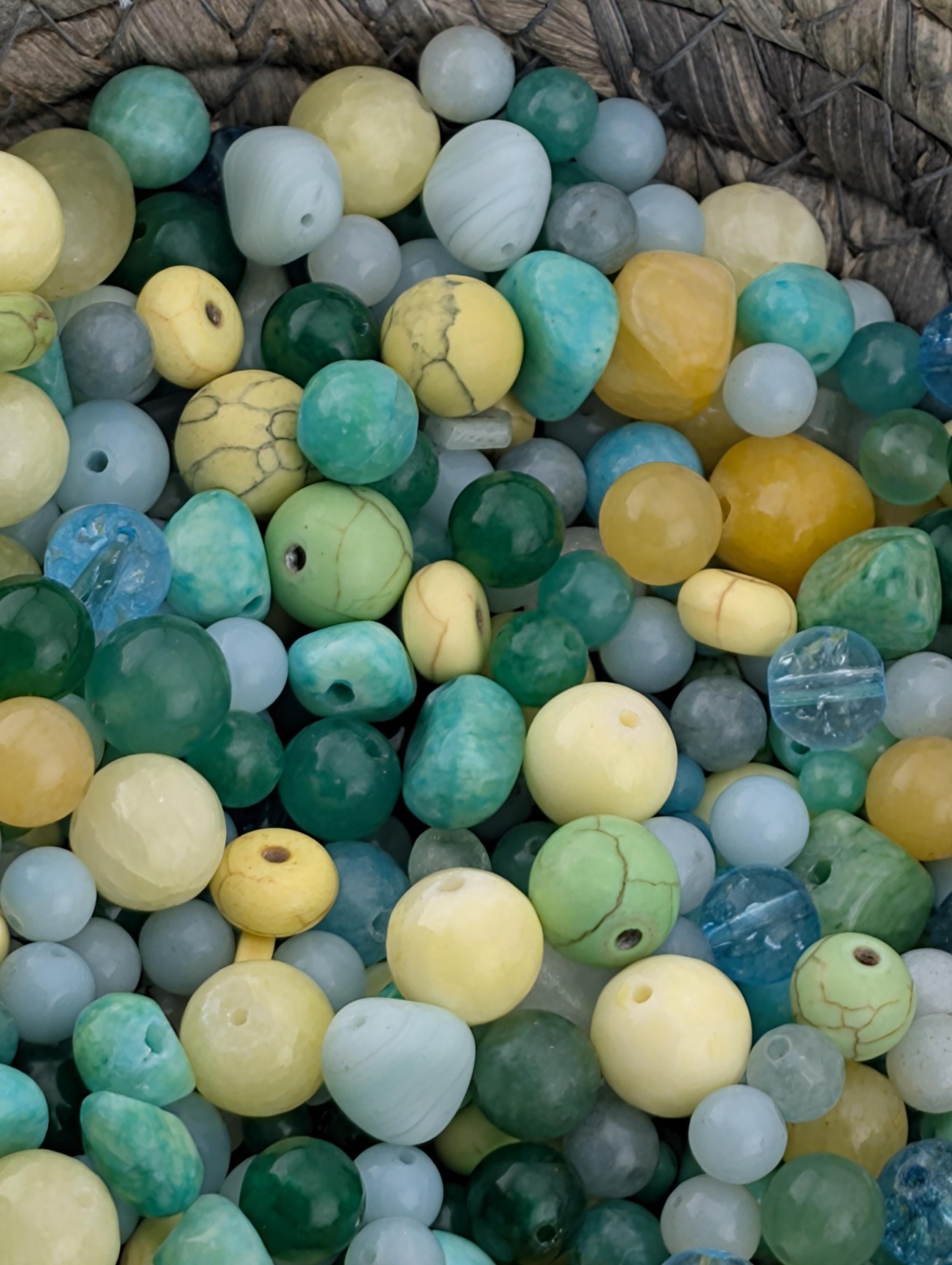 The image is a close-up of a variety of colorful beads and stones, including turquoise, yellow, green, and blue beads, all piled together.