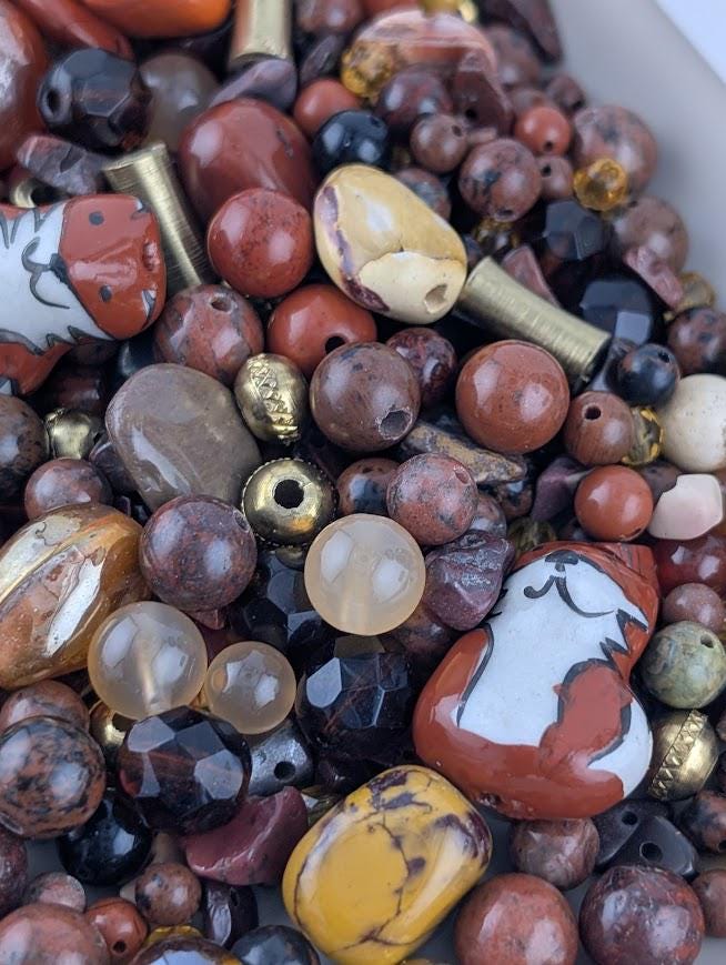The image is a close-up of a variety of colorful beads and stones, including glass beads, metal beads, and natural stones, arranged in a visually appealing manner.