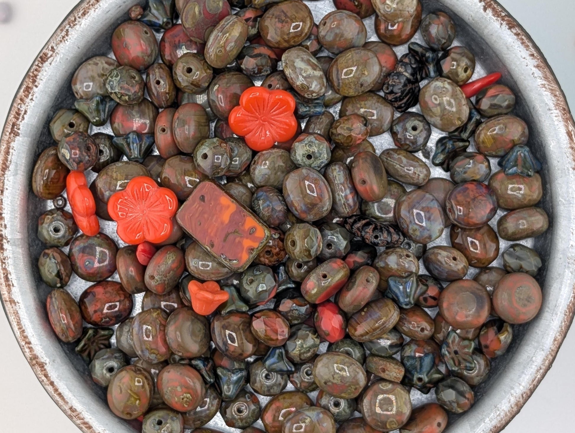 A bowl filled with various colored beads, including red, brown, and black beads, as well as some orange and green beads.