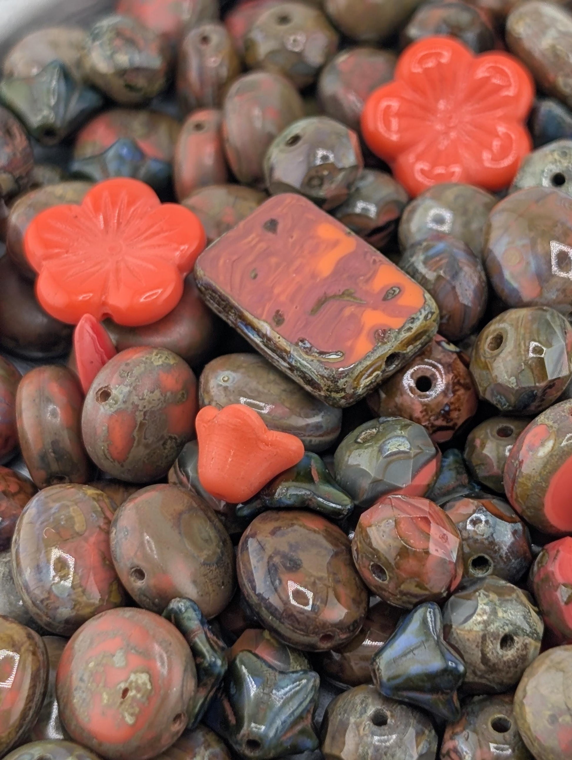 a close-up view of a collection of colorful beads, including red, orange, and brown beads, as well as some larger beads with a flower-like design.