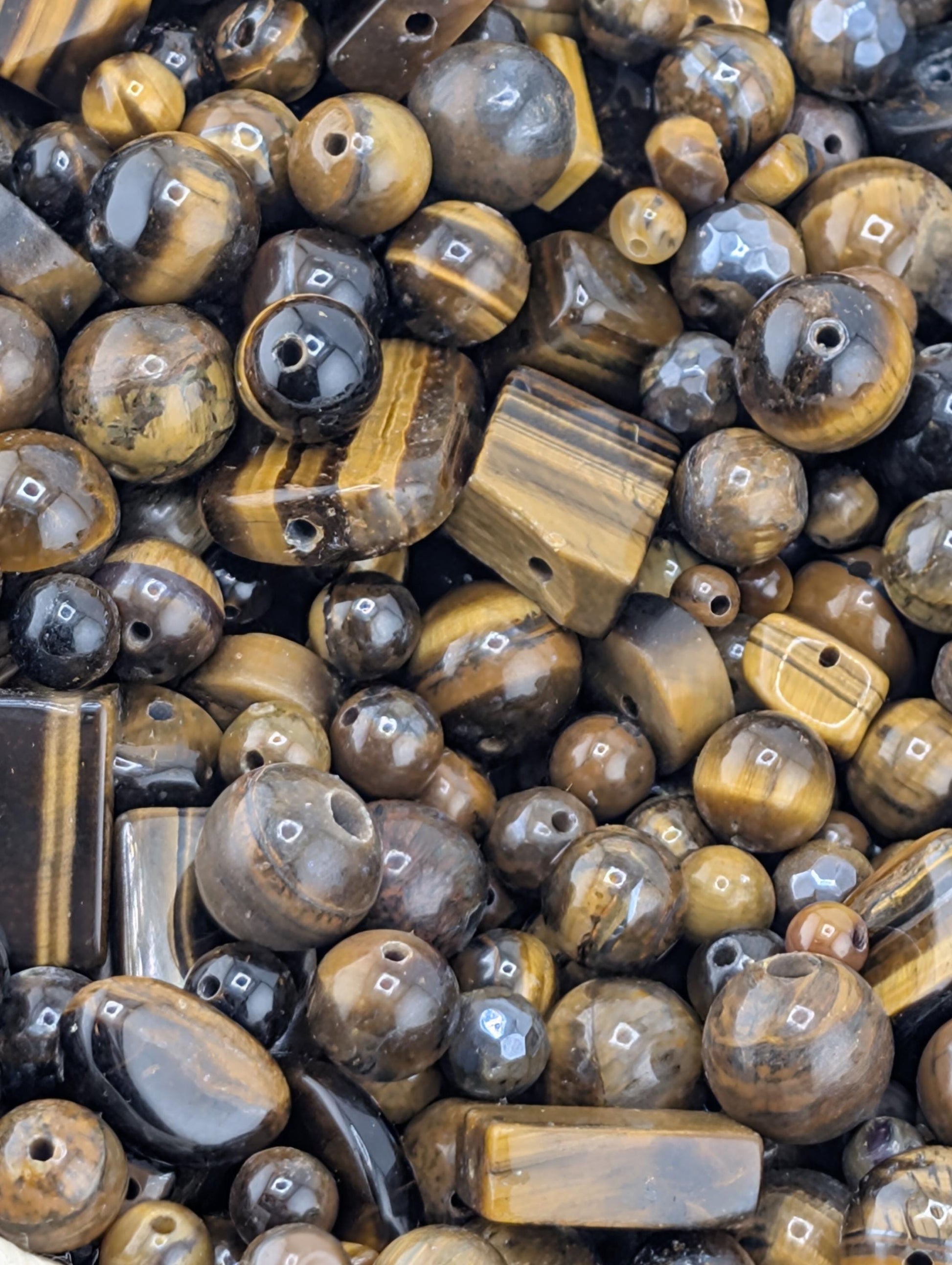 The image is a close-up of various beads and stones, including tiger eye beads, arranged in a pile.