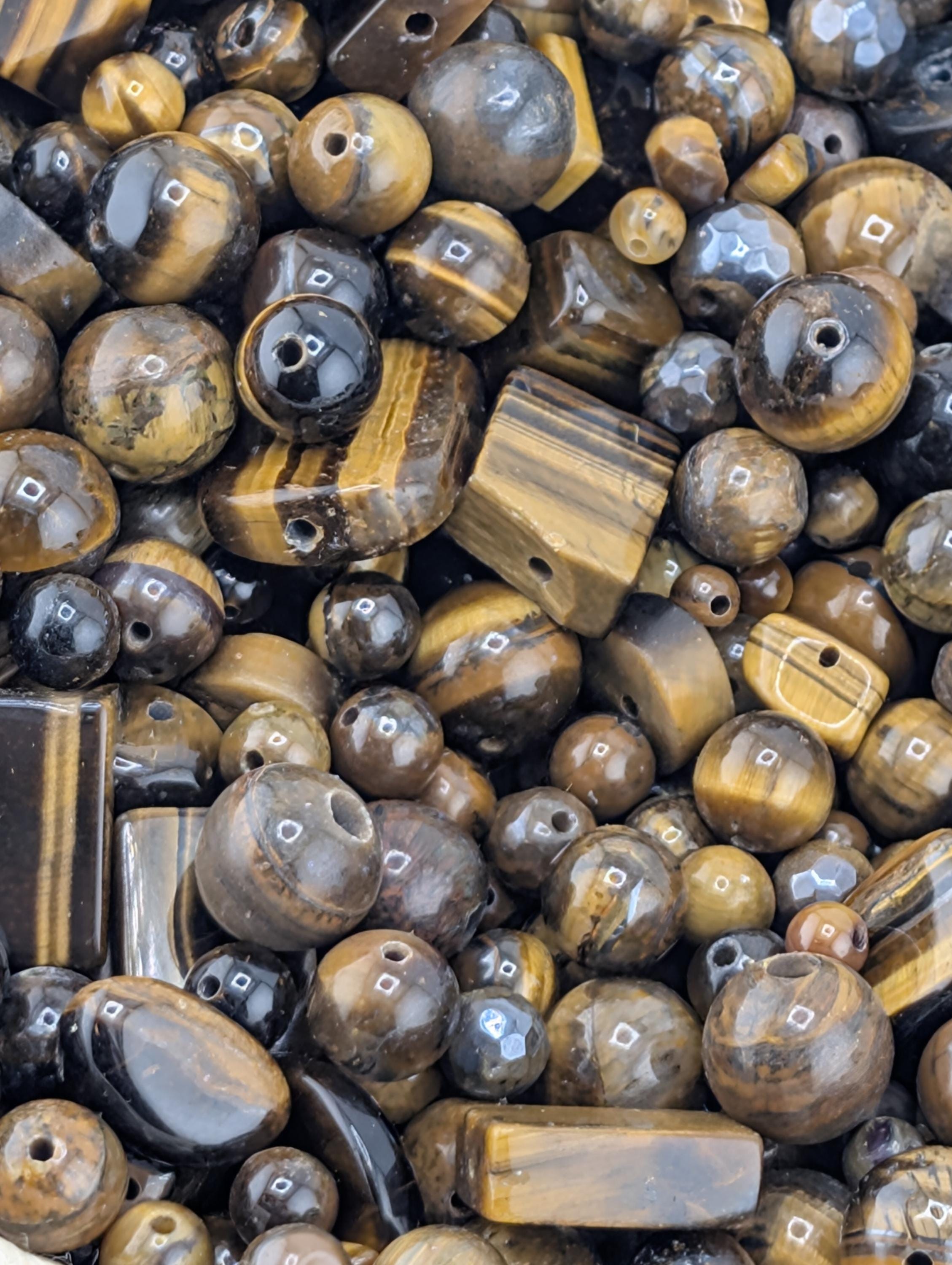 The image is a close-up of various beads and stones, including tiger eye beads, arranged in a pile.