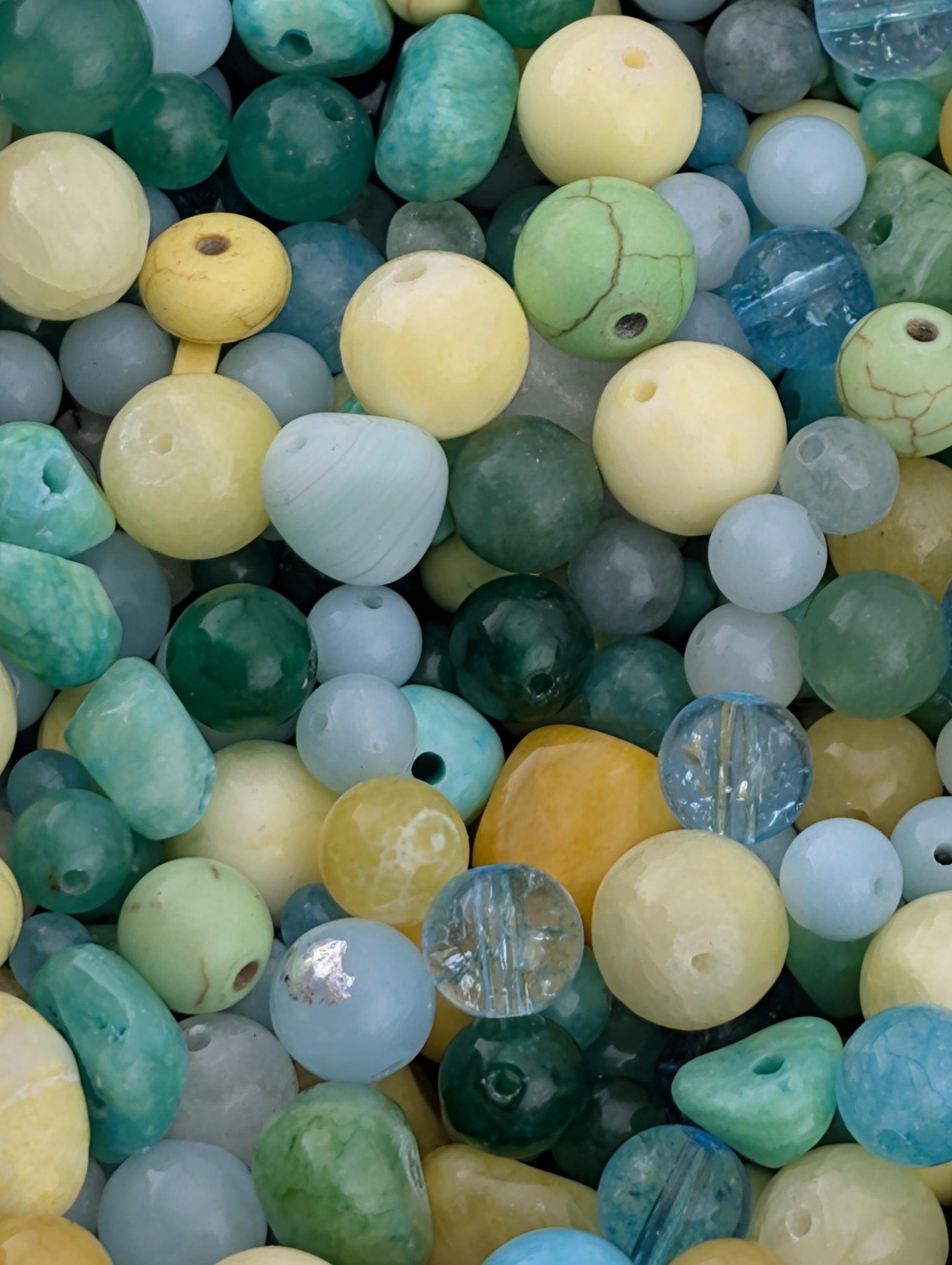 The image is a close-up of a collection of various colored beads, including yellow, green, blue, and turquoise, scattered together.