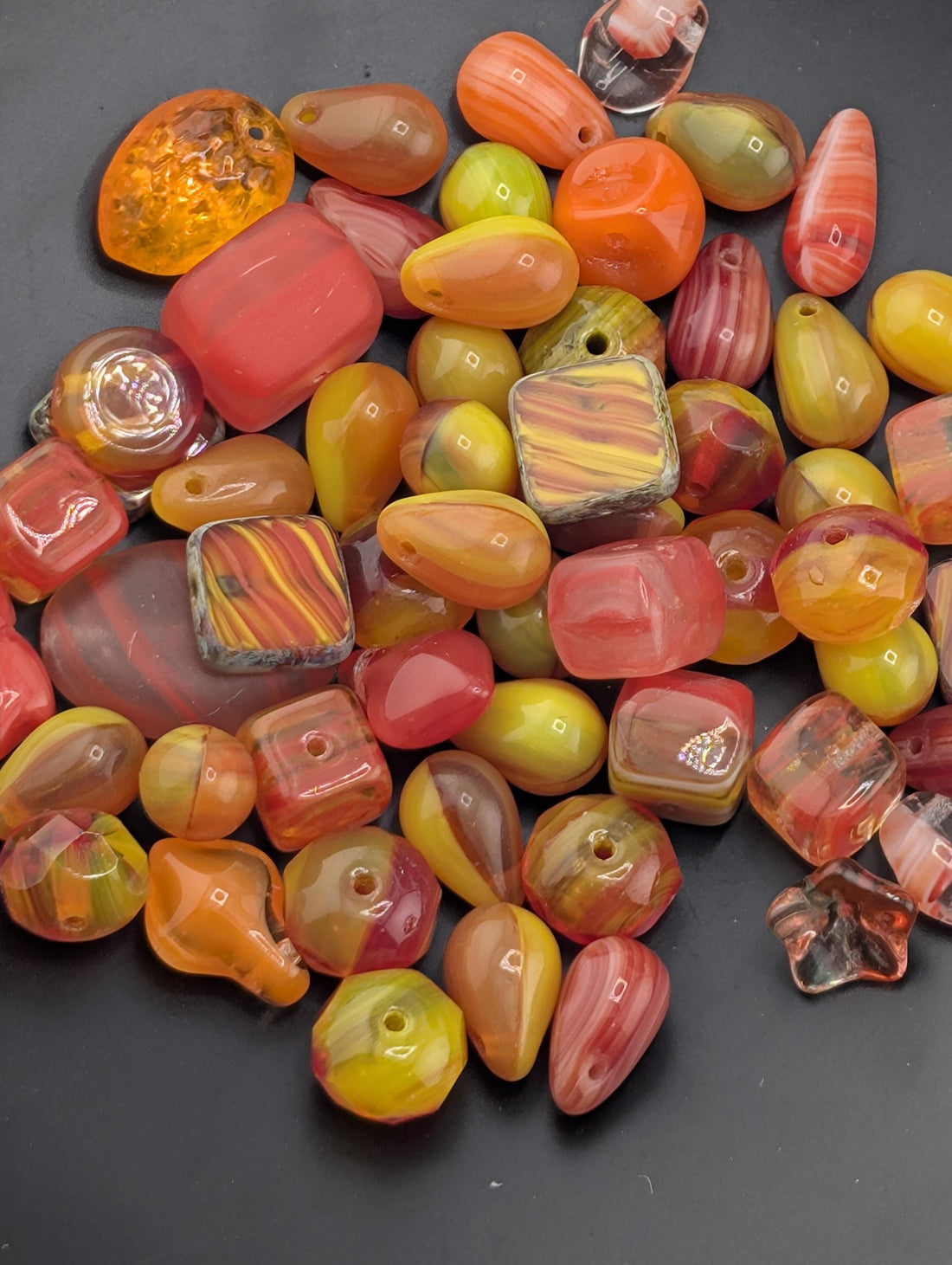 a variety of colorful glass beads, including orange, yellow, and red beads, as well as some clear glass beads. The beads are scattered across a dark surface, creating a visually striking contrast.