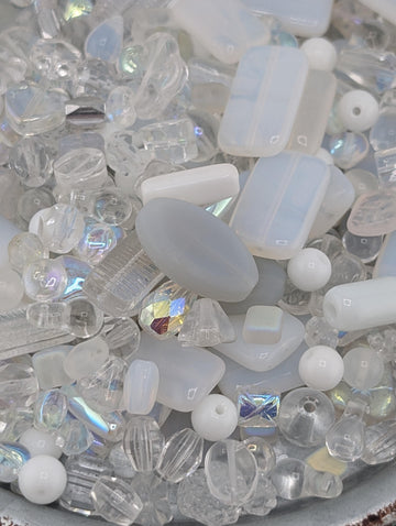 a variety of clear glass beads and crystals, including round, square, and rectangular shapes, scattered together in a visually appealing manner.