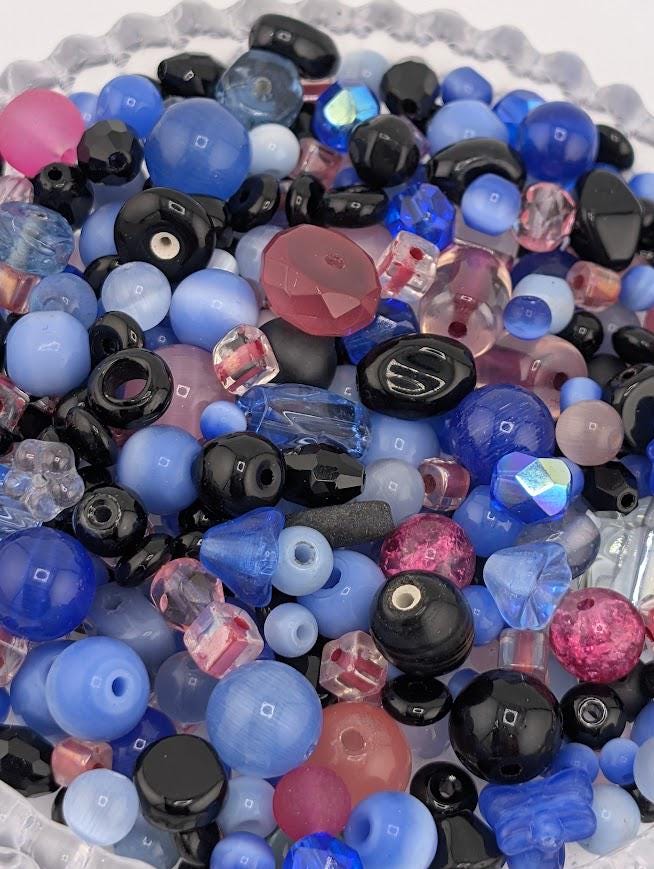 A colorful assortment of various beads, including clear, black, and multicolored glass beads, are scattered together in a bowl.
