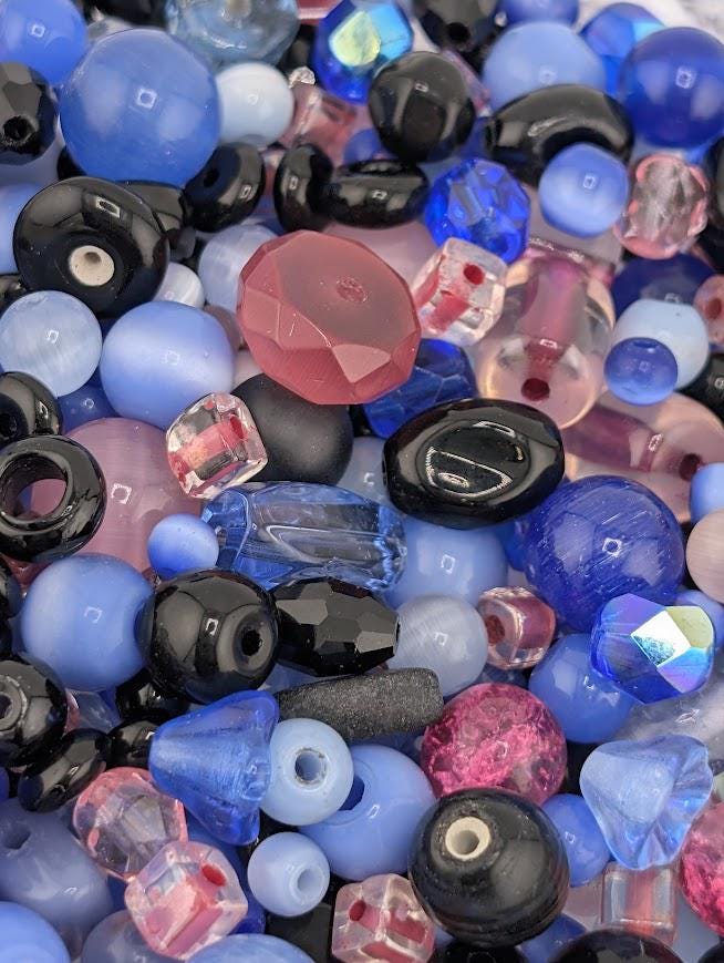 The image is a close-up of various colored glass beads, including blue, black, and pink beads, scattered together.