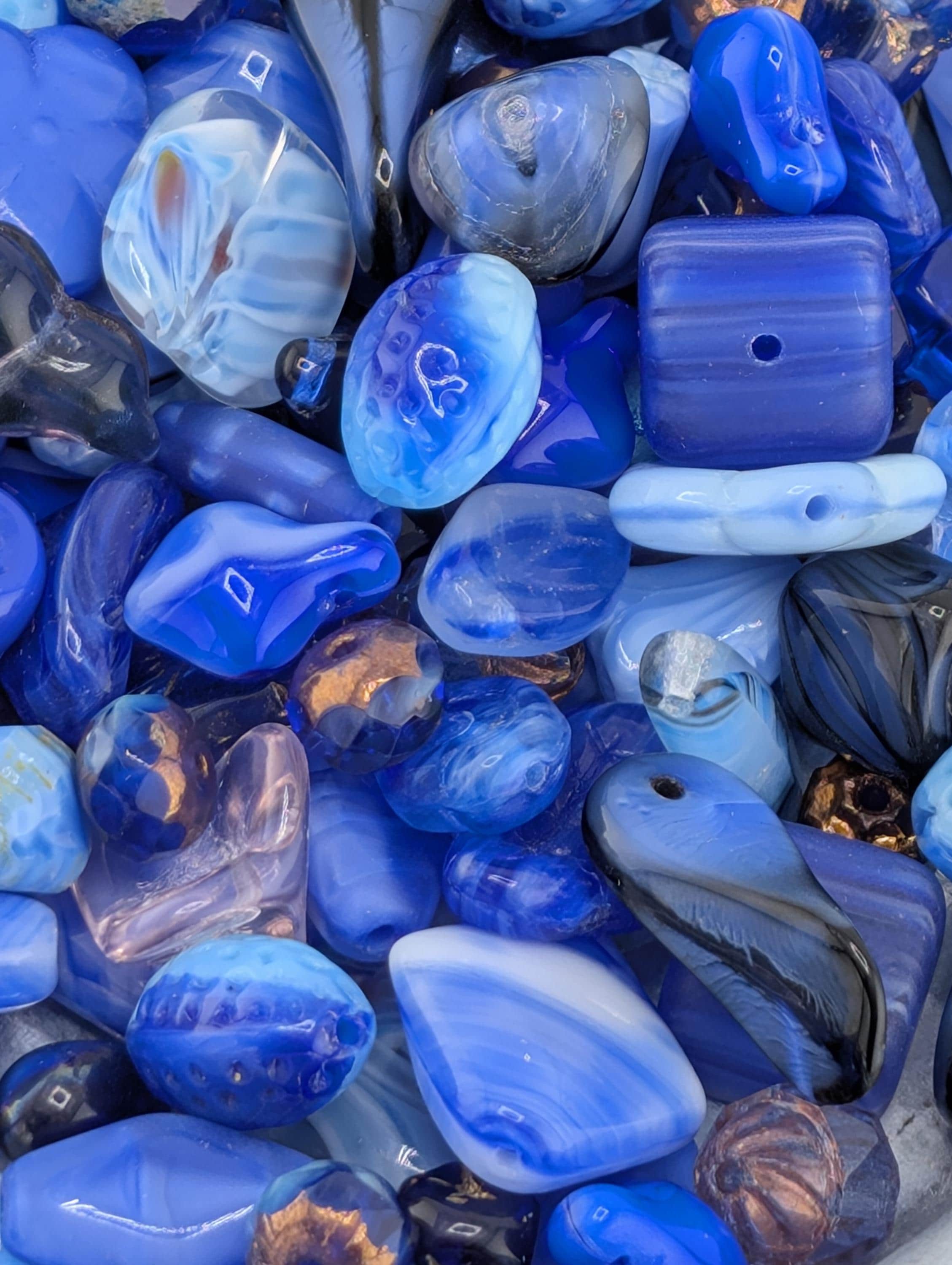The image is a close-up of various blue and purple glass beads, showcasing their intricate patterns and textures.