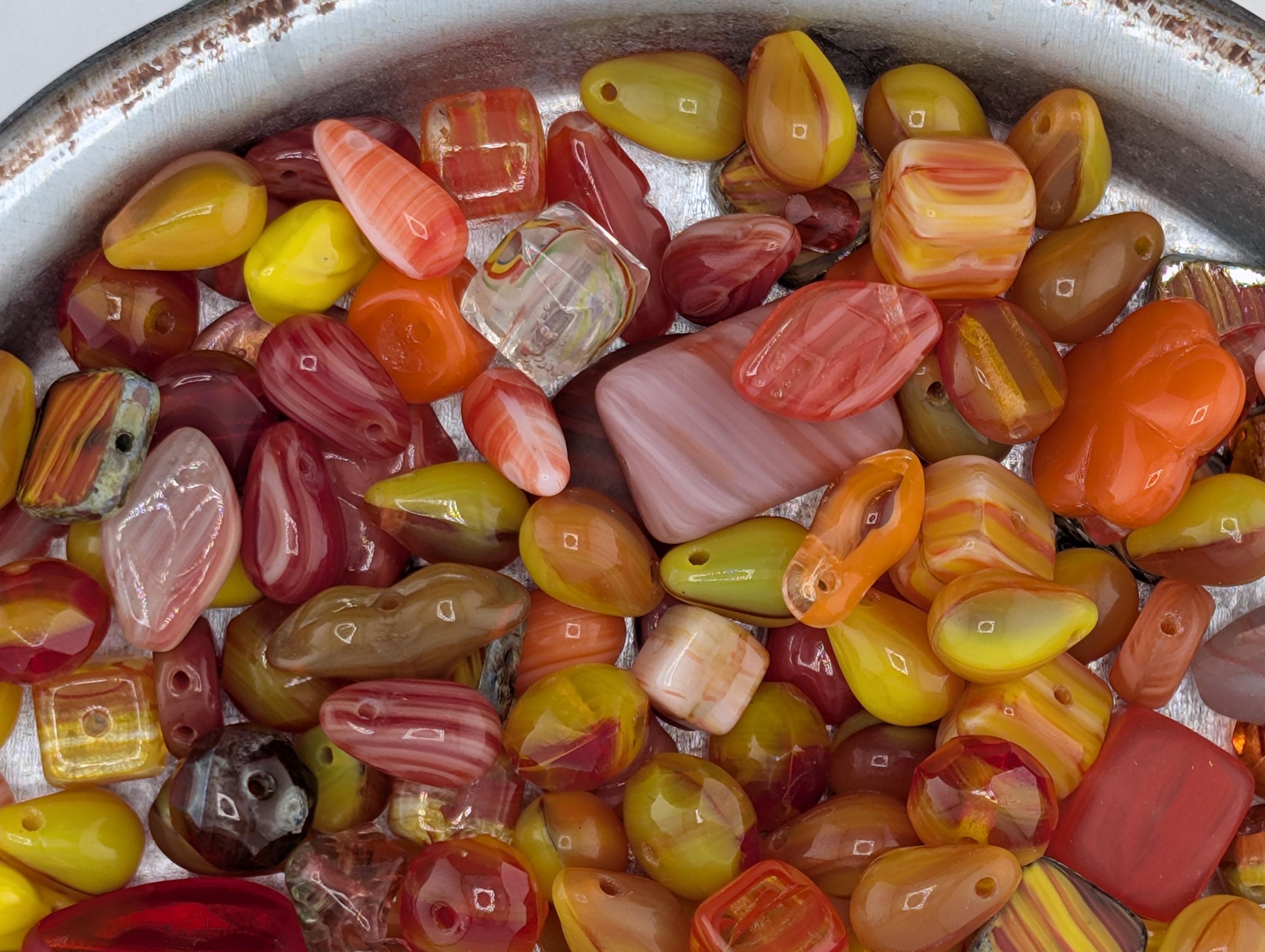 A close-up image of a variety of colorful beads, including glass beads and plastic beads, scattered together in a container.