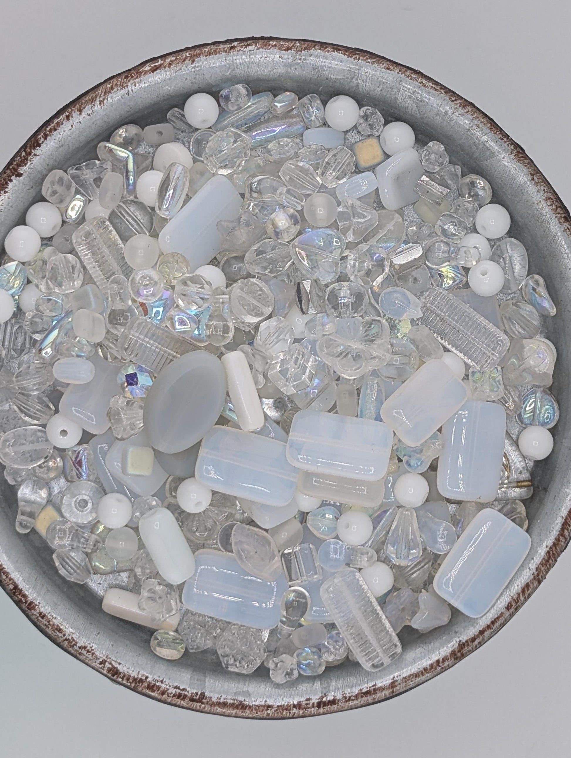 A bowl filled with various clear glass beads in different shapes and sizes, creating a visually appealing and diverse collection.