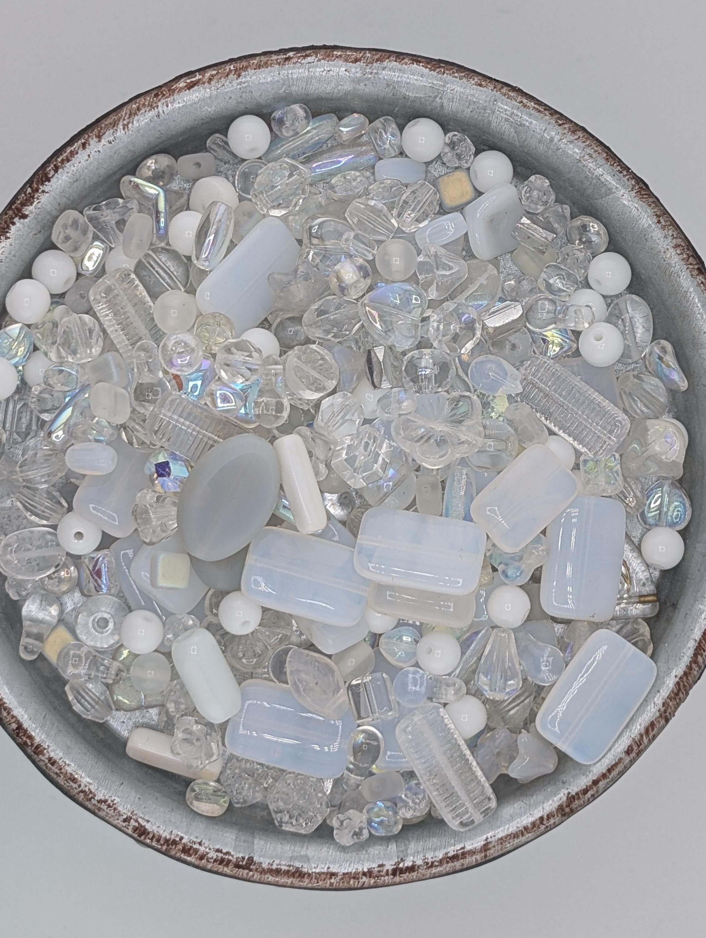 A bowl filled with various clear glass beads in different shapes and sizes, creating a visually appealing and diverse collection.