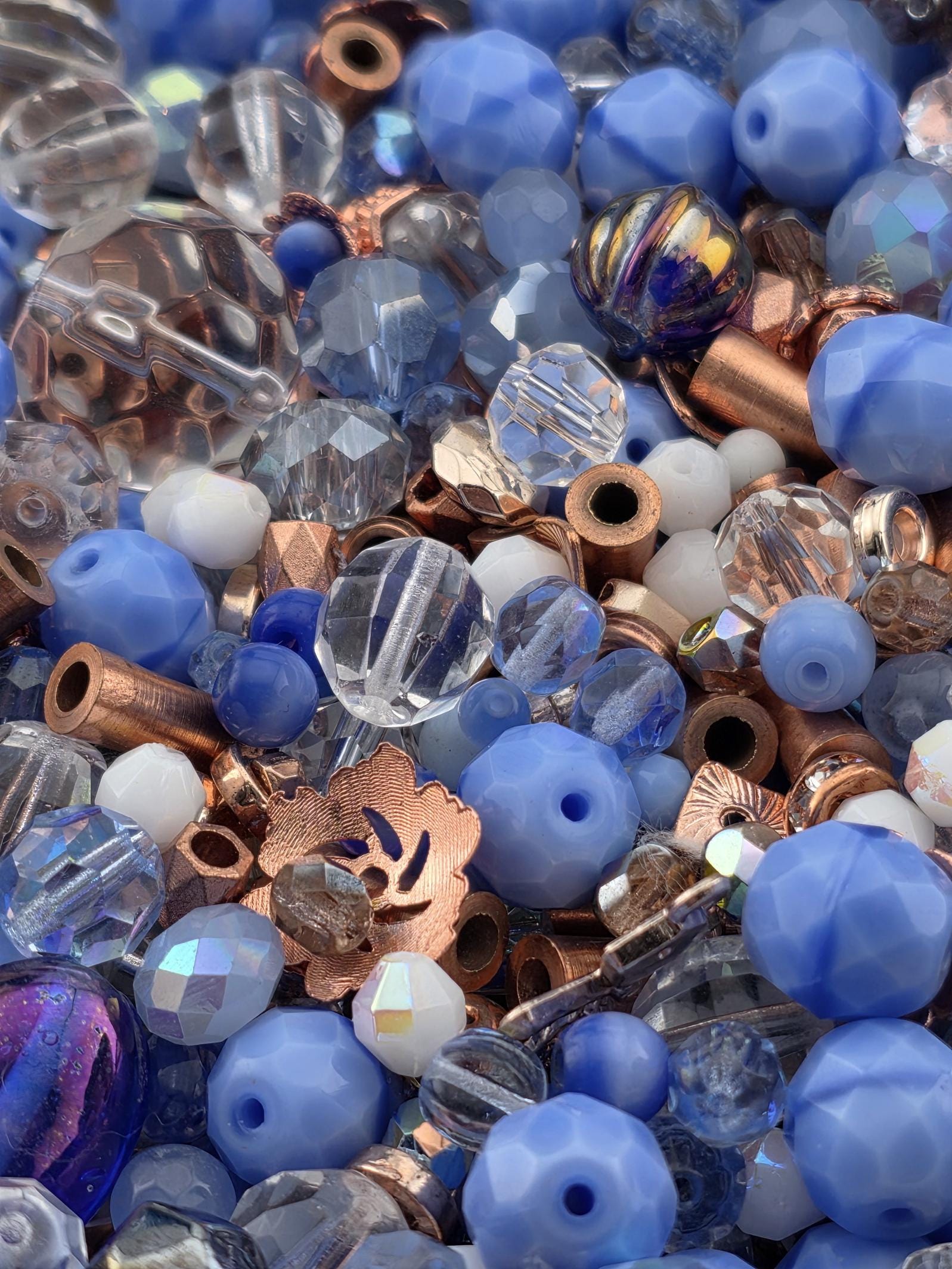 The image is a close-up of various beads and metal pieces, including clear, blue, and copper-colored beads, as well as metal rods and other metallic components.