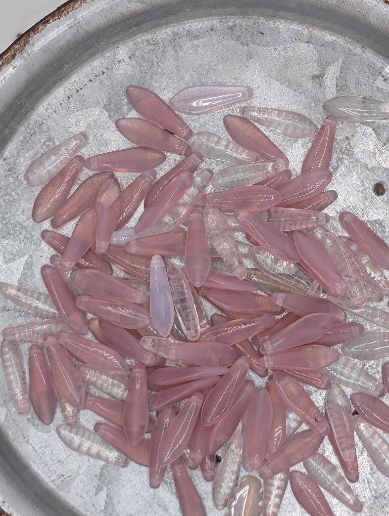 a collection of small, clear beads in various shades of pink and white, scattered on a metal surface.