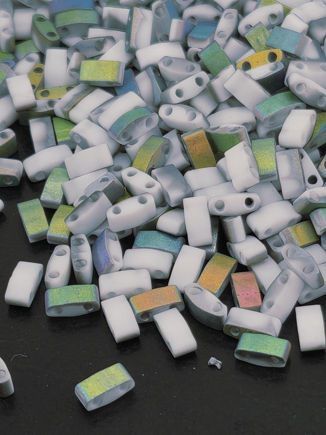 The image is a close-up of a pile of small, colorful beads or objects scattered on a dark surface.