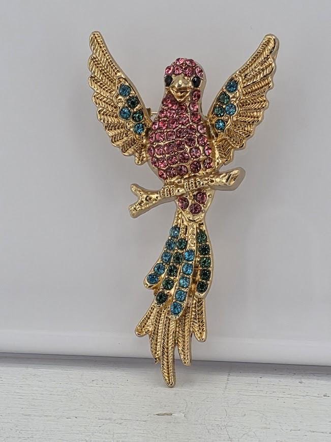 A decorative gold-colored pin or brooch in the shape of a bird, adorned with colorful gemstones.