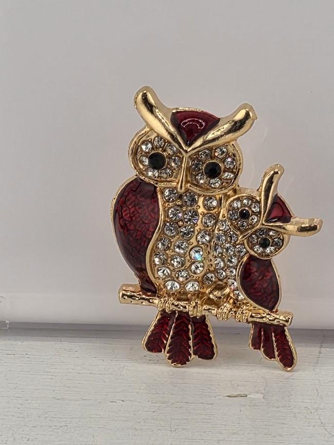 A decorative brooch in the shape of two owls, with one owl being larger and the other smaller, both adorned with gemstones.