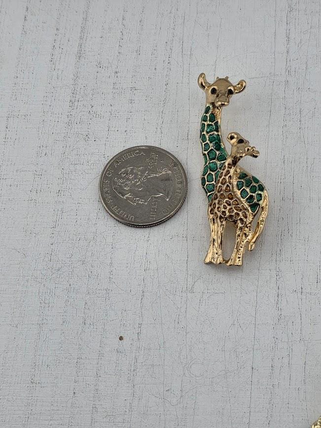 A small gold-colored giraffe brooch is placed next to a silver coin on a white surface.