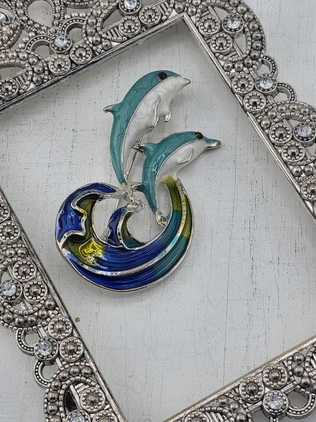 A decorative metal frame with a blue and white dolphin brooch on top, placed on a white surface.