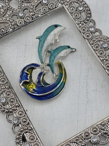 A decorative metal frame with a blue and white dolphin brooch on top, placed on a white surface.
