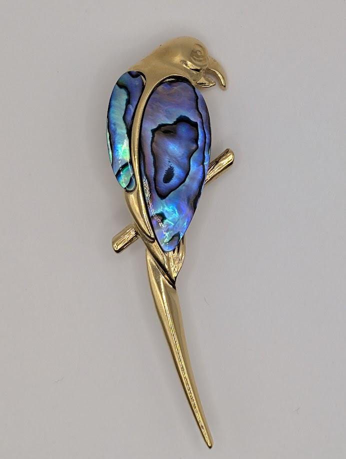A gold-colored bird brooch with a blue and purple iridescent feather design.