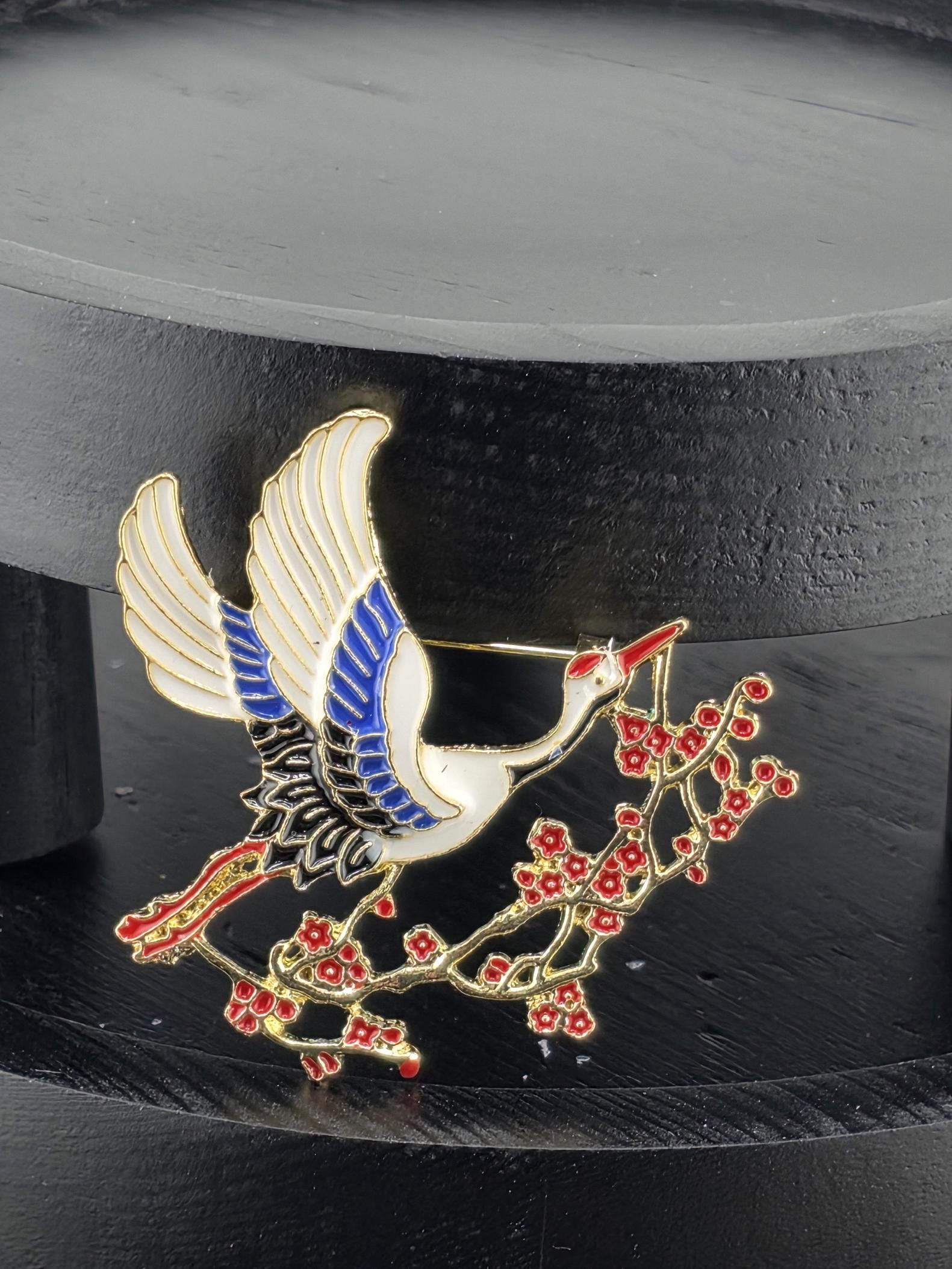 A close-up of a decorative metal piece featuring a stylized bird in flight, with a branch of red flowers or berries attached to it.