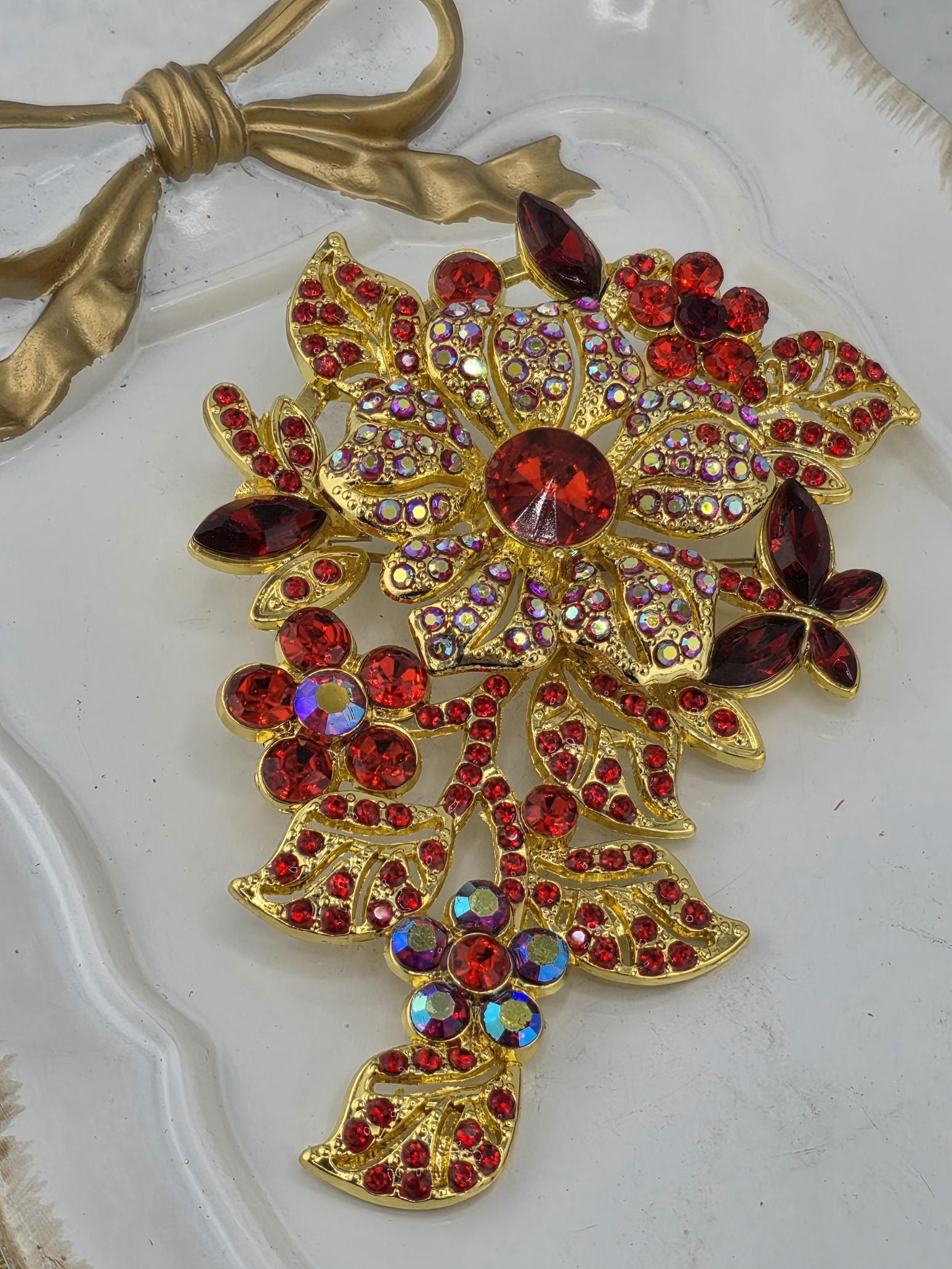 a decorative piece of jewelry with a combination of red and gold elements, including a large red gemstone surrounded by smaller red gemstones and gold leaves.