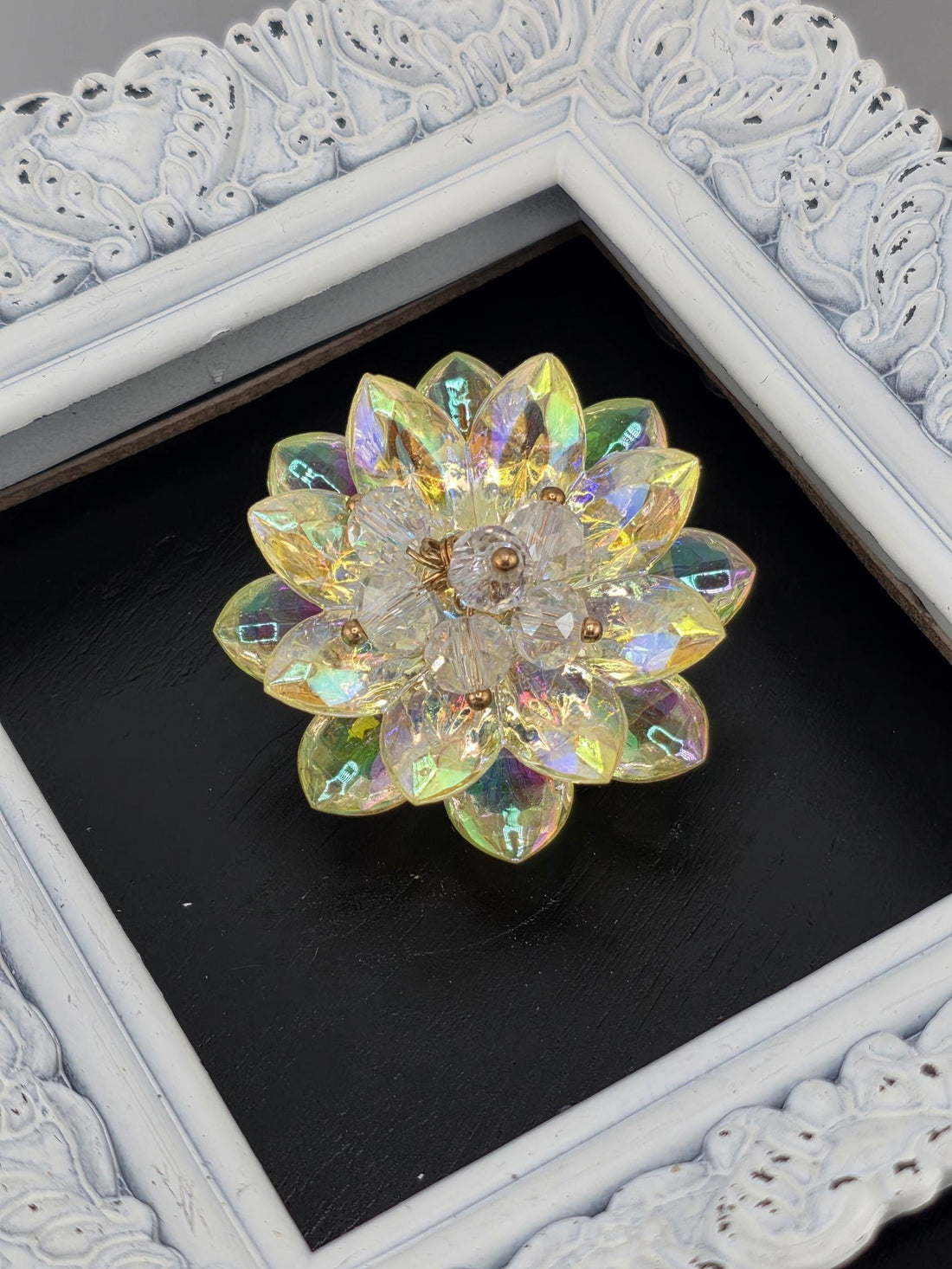 A decorative crystal flower-shaped object is displayed in a white ornate frame against a black background.
