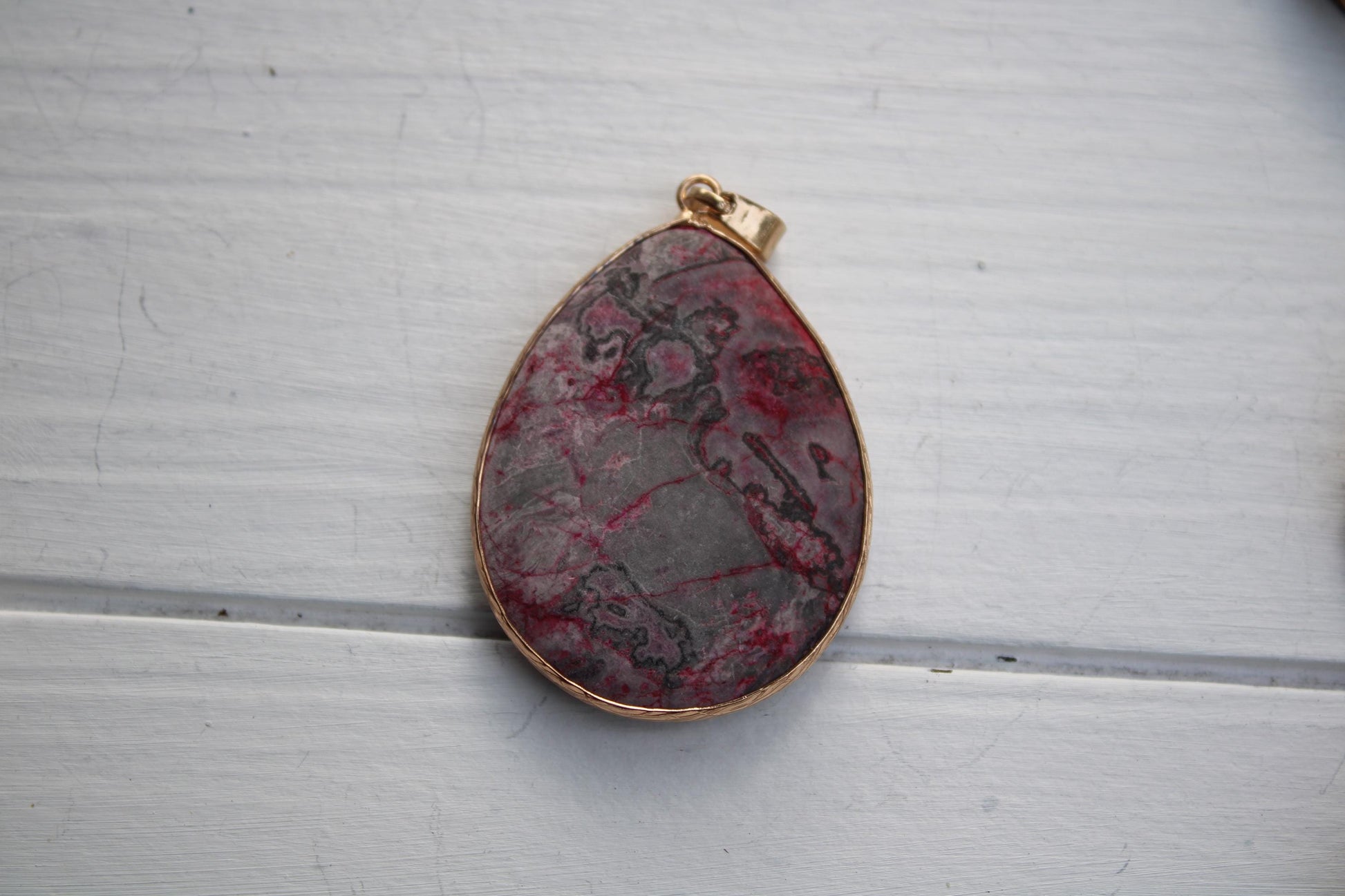 A pendant with a red and gray stone-like design, possibly a type of rock or gemstone, is displayed on a white wooden surface.