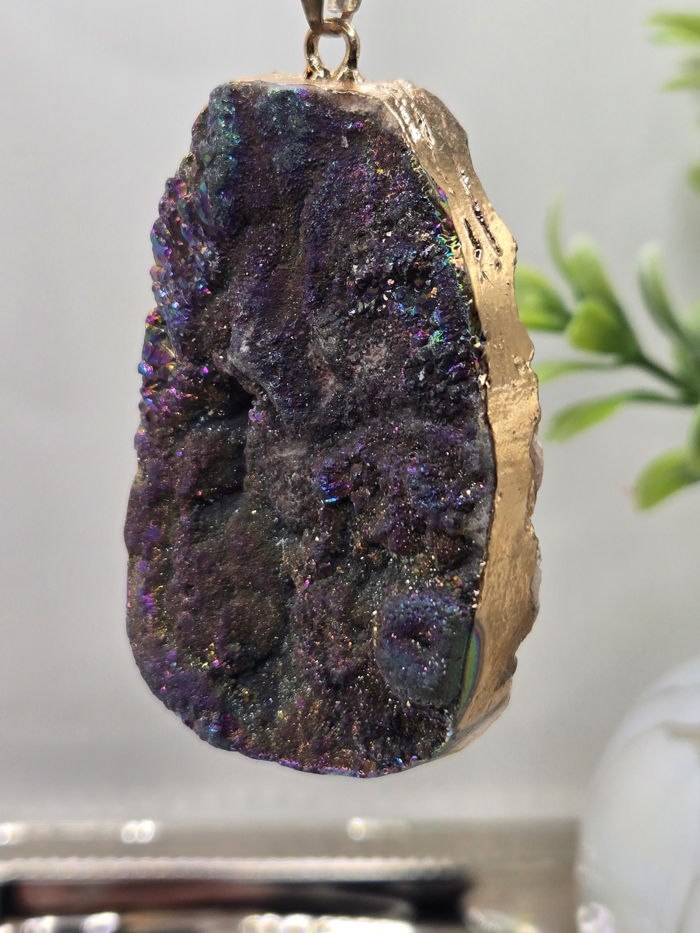 A close-up image of a piece of purple and blue gemstone with a gold-colored border, hanging from a chain.