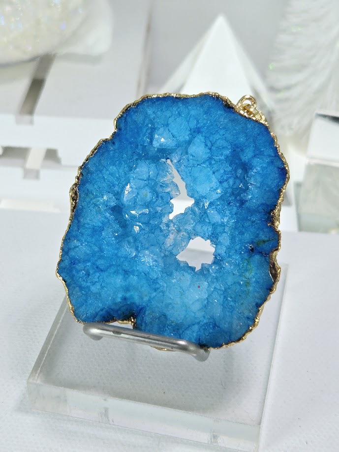 A close-up image of a blue geode with a gold-colored base, displayed on a clear stand.