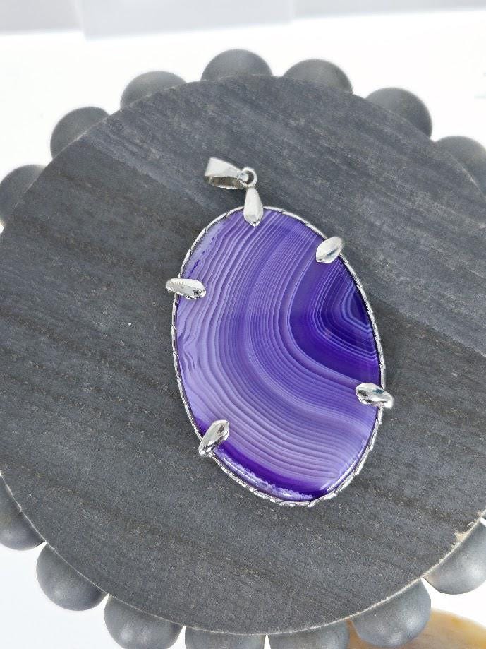 A purple agate stone with a silver pendant is displayed on a white surface.