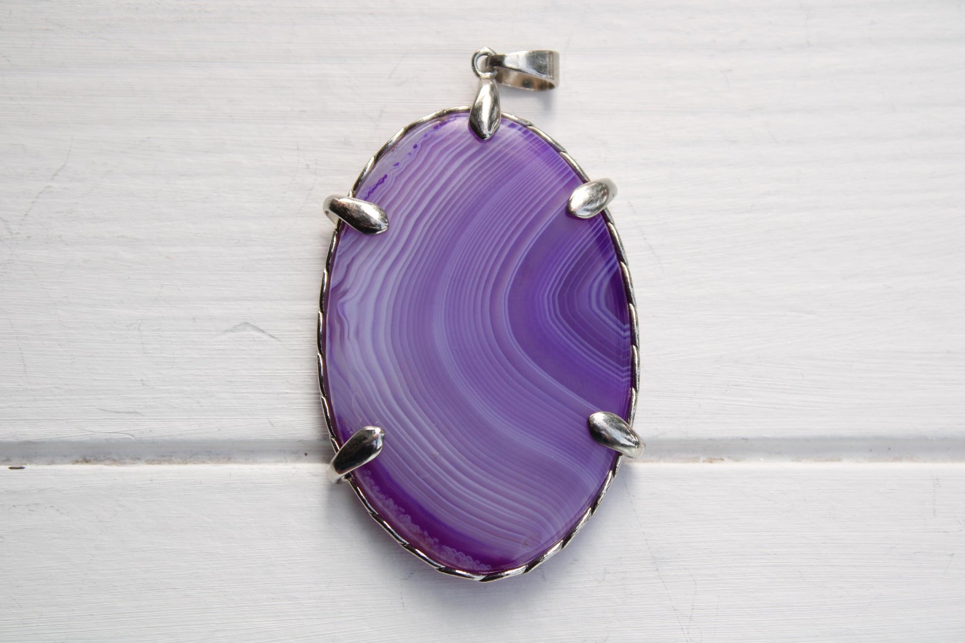 A large oval-shaped purple stone with a silver frame, hanging on a white surface.