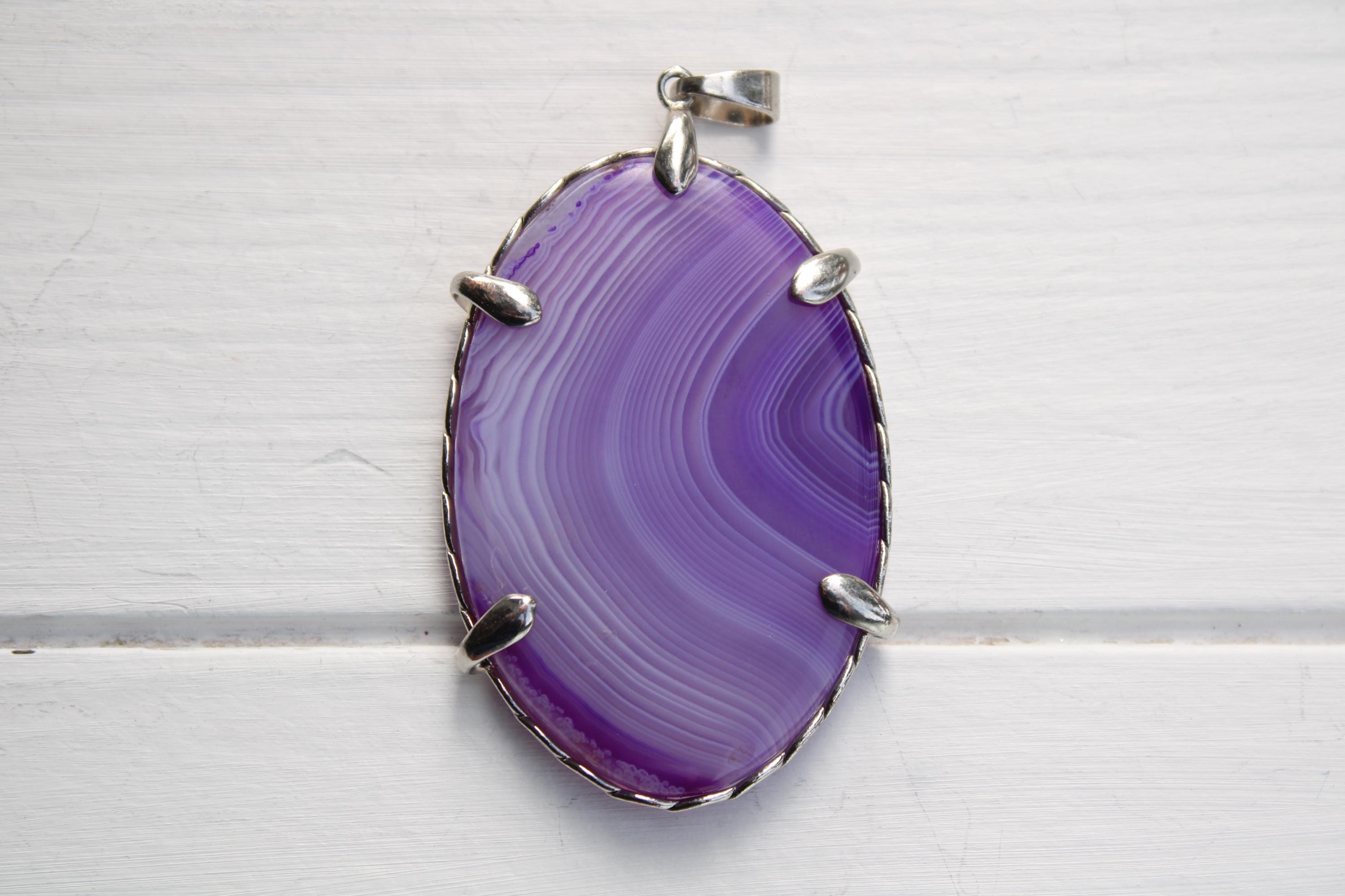 A large oval-shaped purple stone with a silver frame, hanging on a white surface.