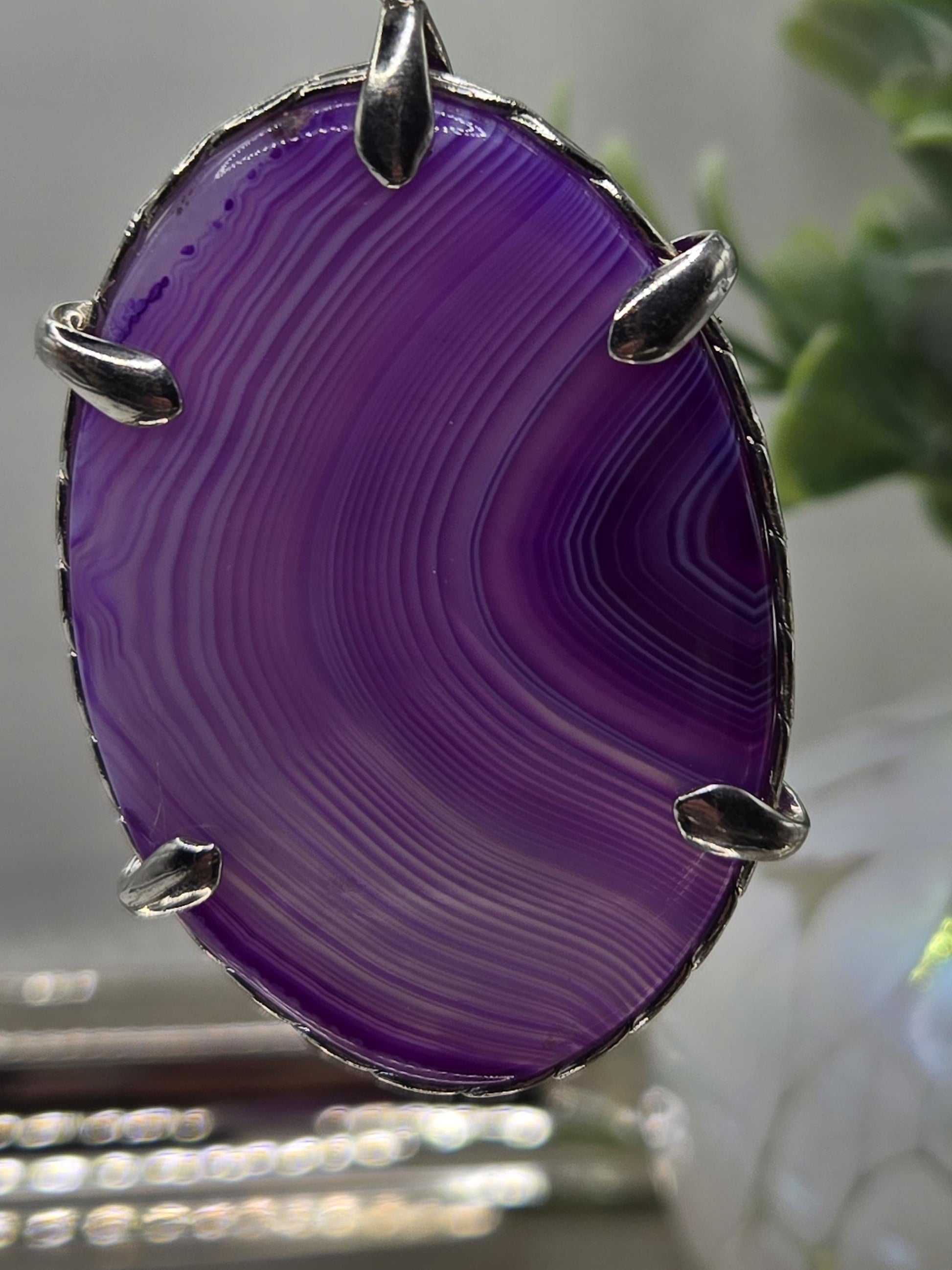 A close-up image of a purple stone with a unique striped pattern, mounted on a metal frame with metal claws.