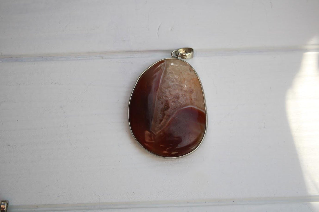 a large, oval-shaped stone with a unique, multicolored pattern, possibly a piece of natural rock or gemstone. The stone is attached to a silver-colored pendant or charm, which is hanging from a chain or cord.