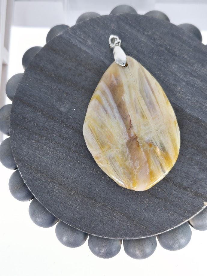 A pendant made of a yellowish-brown stone, possibly a type of amber or fossil, is displayed on a gray circular stand.