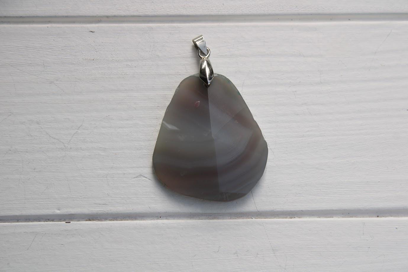 A pendant made of a dark-colored stone, possibly a type of agate, is hanging on a white wooden surface.