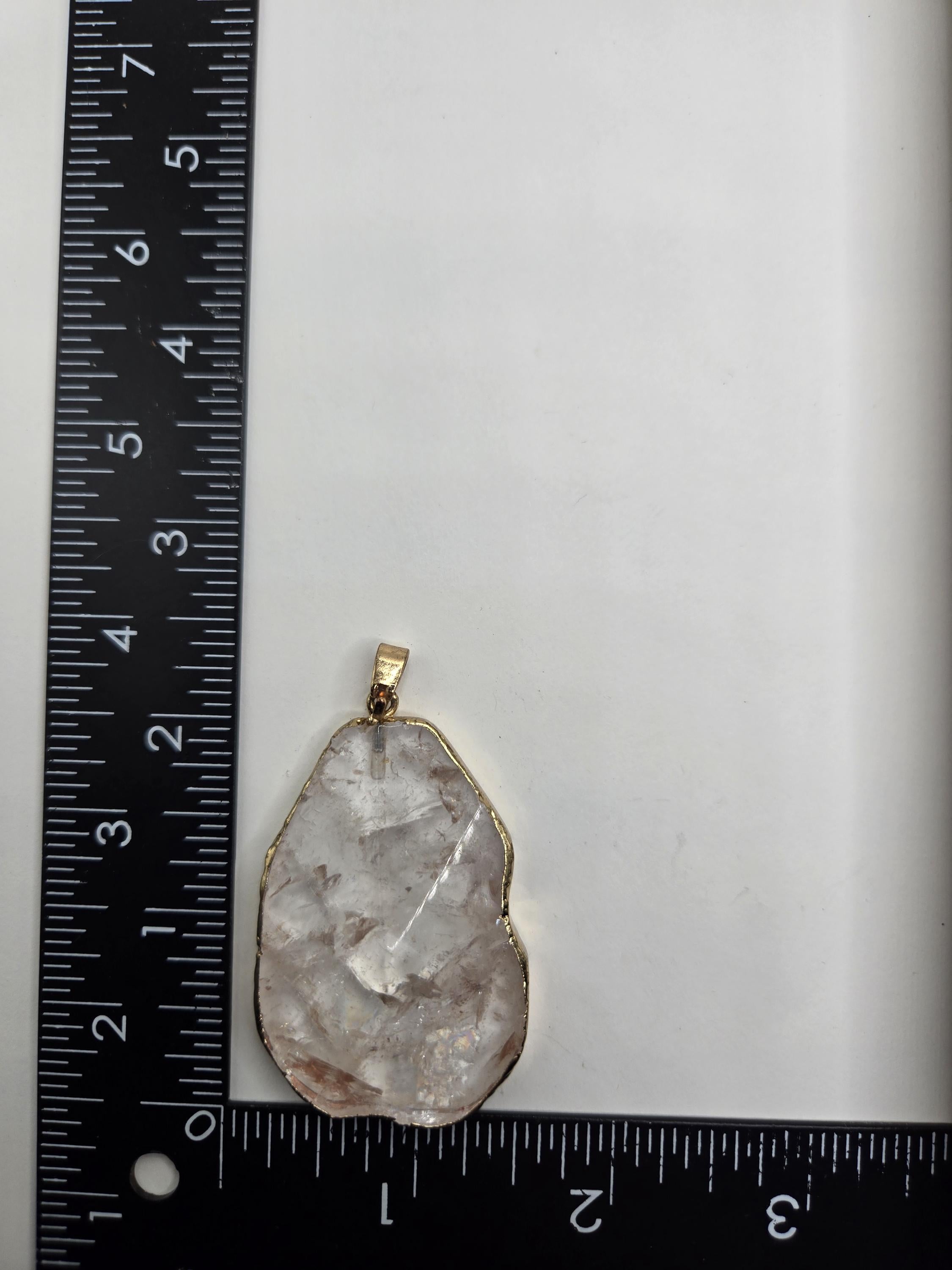 A clear crystal pendant is placed next to a ruler on a white surface.
