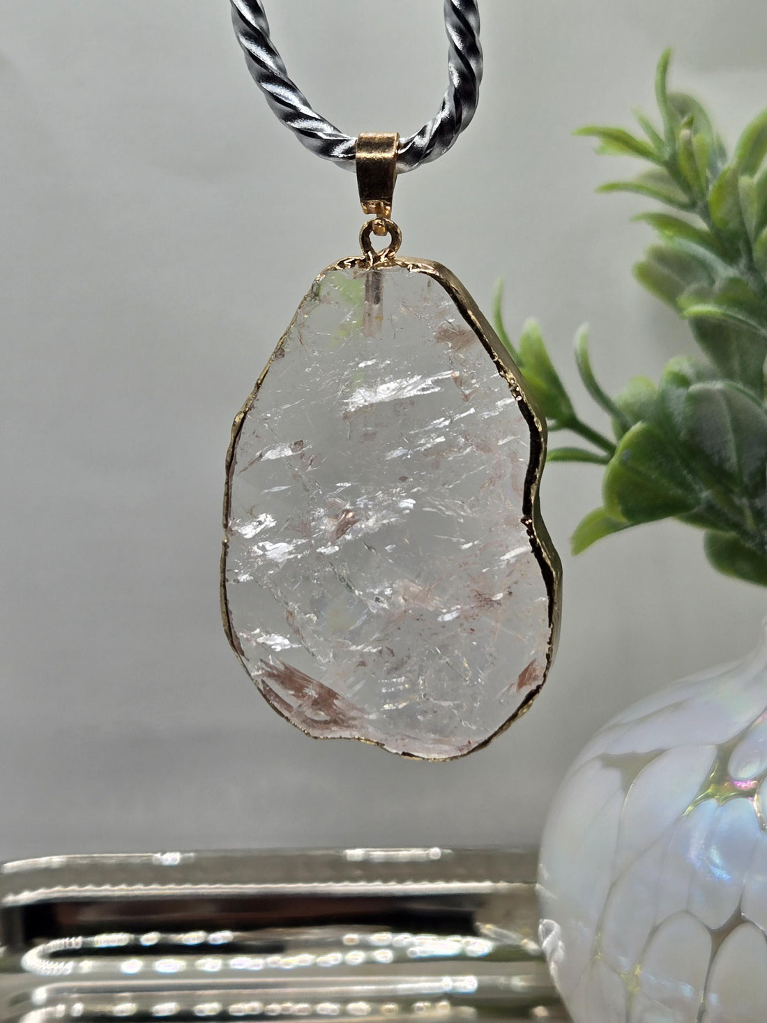A large, clear crystal pendant with a gold-colored frame hangs from a silver chain.
