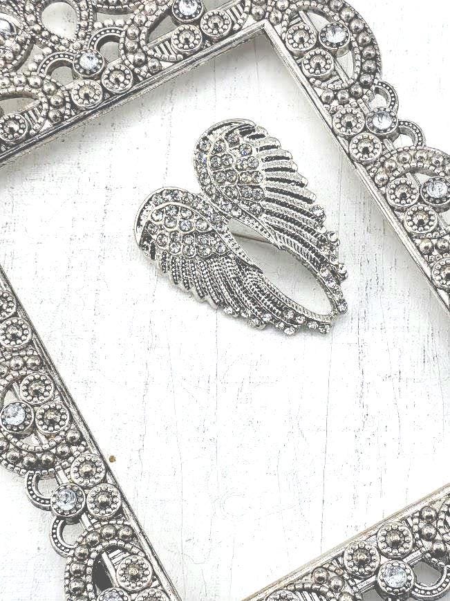 A silver-colored ornate frame with a decorative border, featuring a pair of intricately designed wings as the focal point.