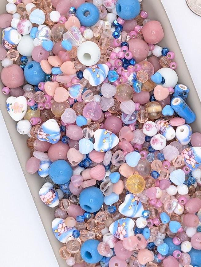 A colorful assortment of glass beads in various shades of pink, blue, and white, scattered across a surface.