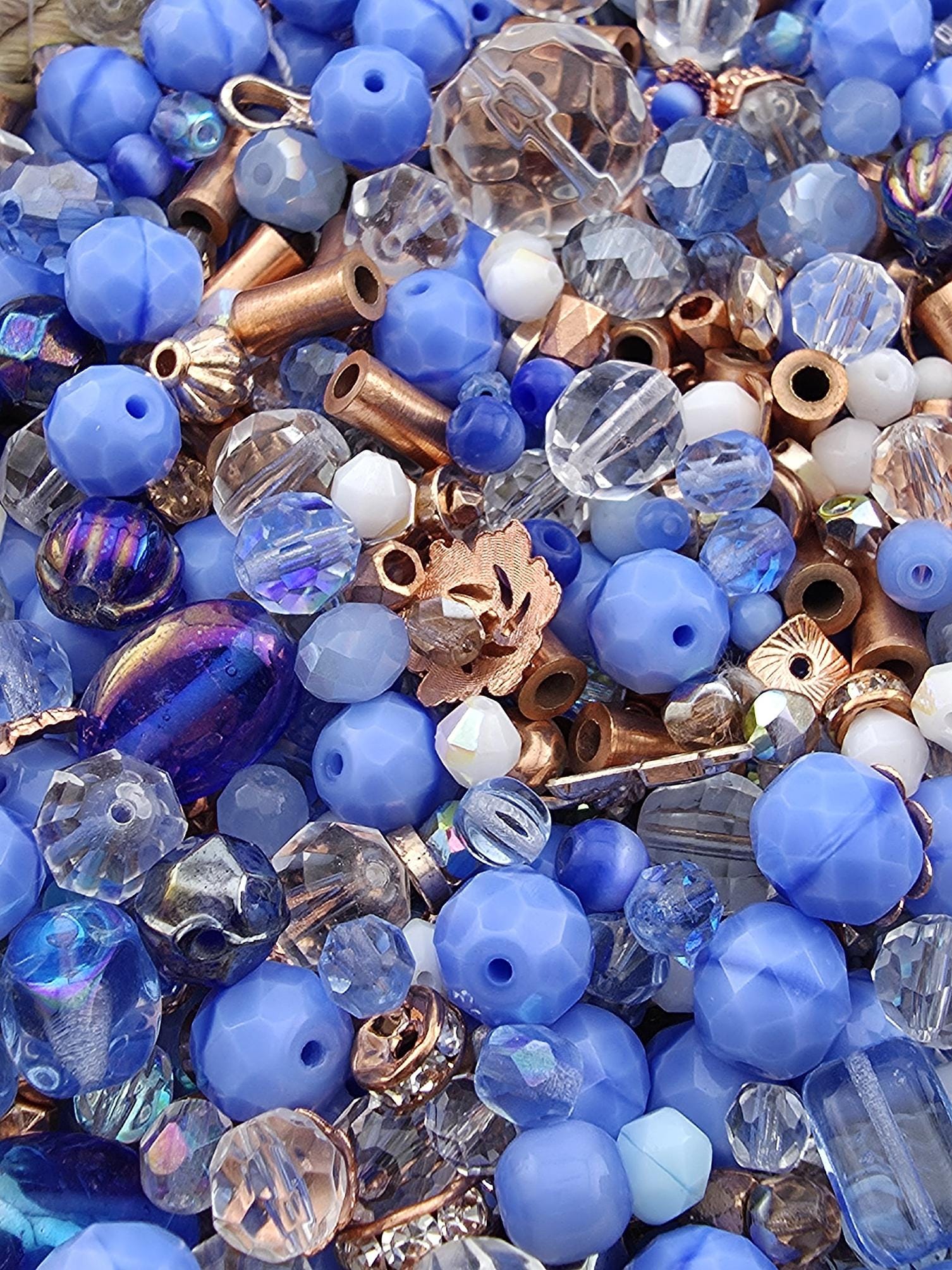 The image is a close-up of various beads and metal pieces, including clear and blue beads, copper-colored beads, and some metallic components.