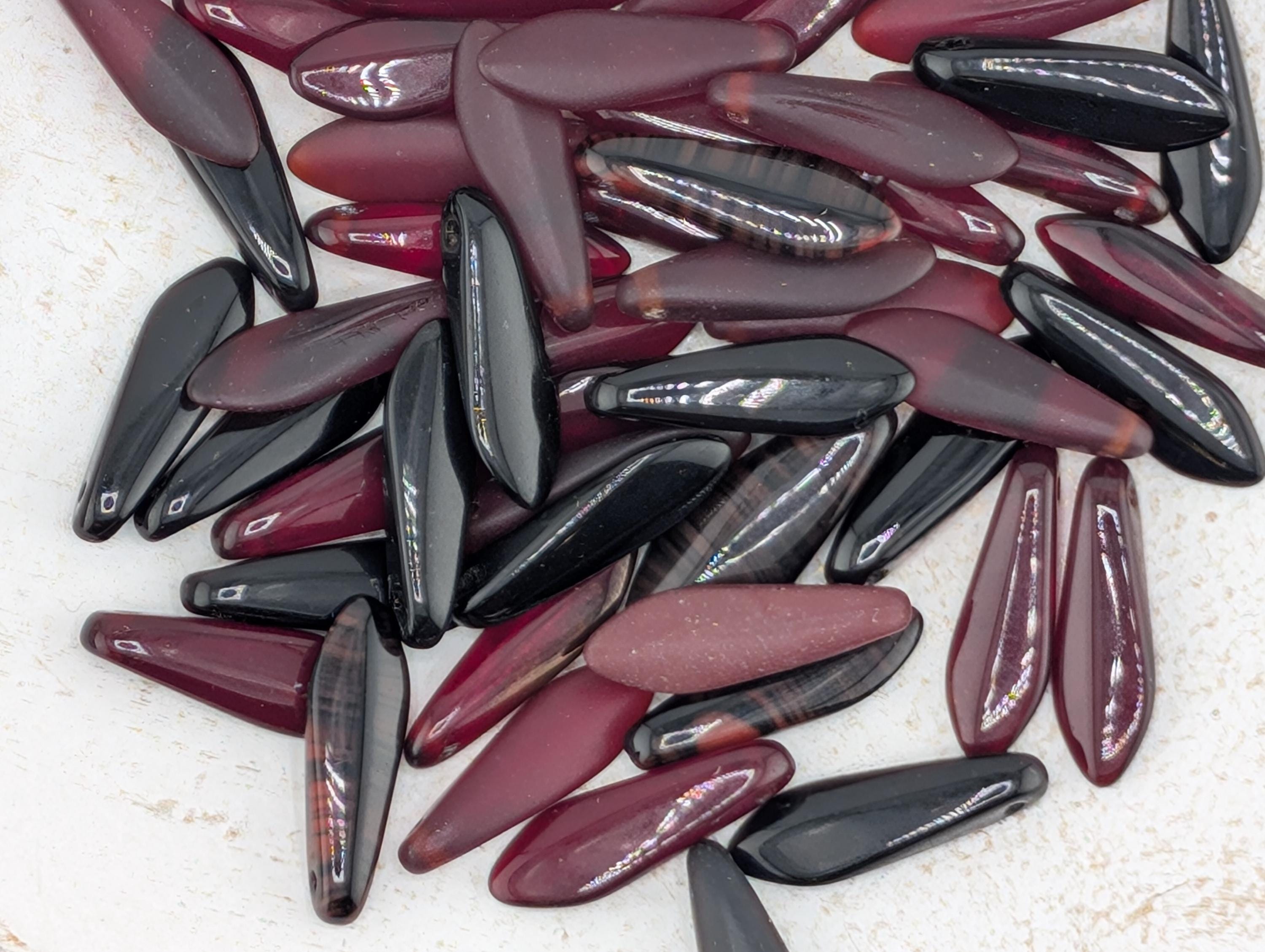a collection of various colored glass beads, including maroon, black, and red, scattered on a white surface.