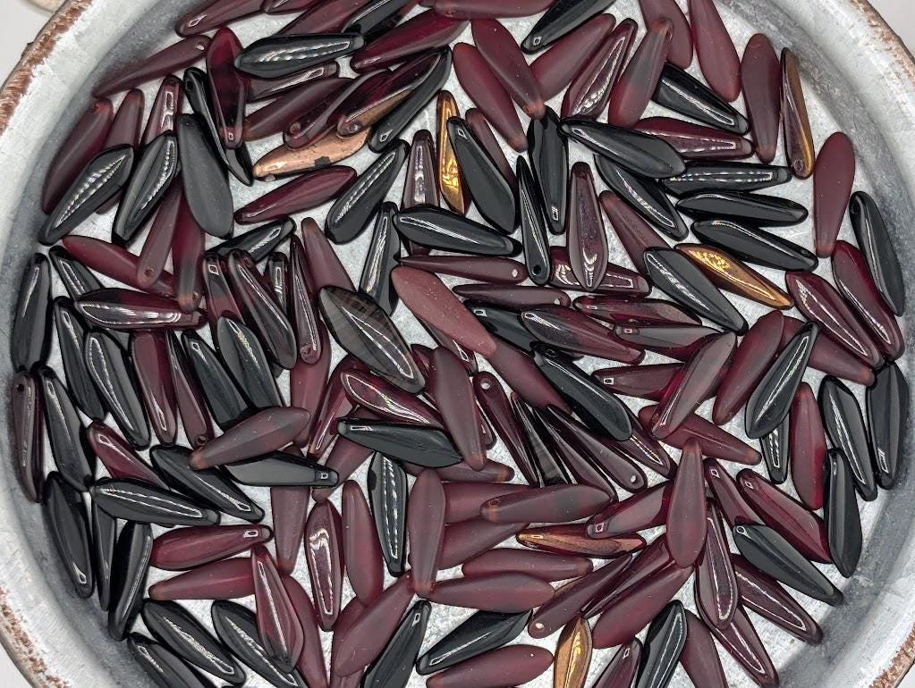 a close-up view of a collection of various colored glass beads, including maroon, black, and gold, arranged in a circular pattern.