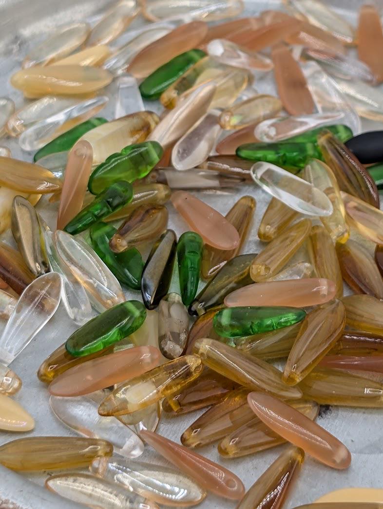 a collection of various colored glass beads, including clear, green, and brown, scattered on a surface.