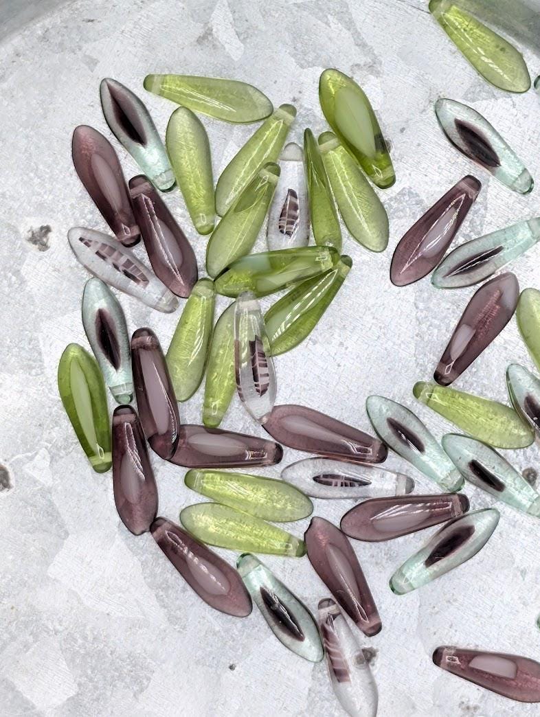 a collection of various colored glass beads, including green, purple, and clear beads, scattered on a surface.