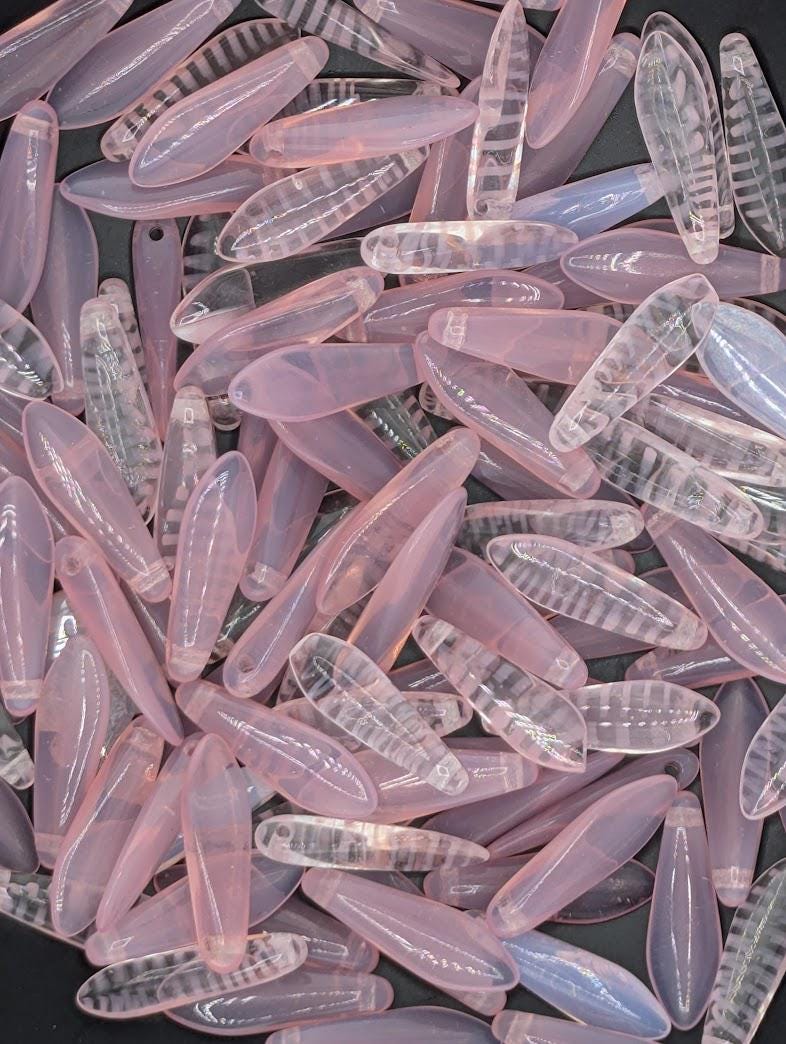 numerous clear, translucent beads in various shades of pink and purple, scattered across a dark background.
